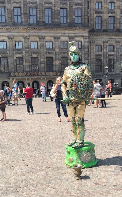 A green living-statue street performer with a painted shield standing motionless on Dam Square