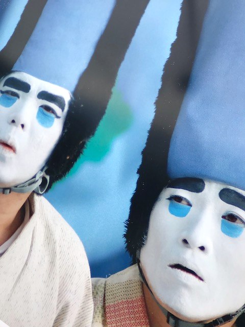 Two street performers in tall blue hats and white painted masks